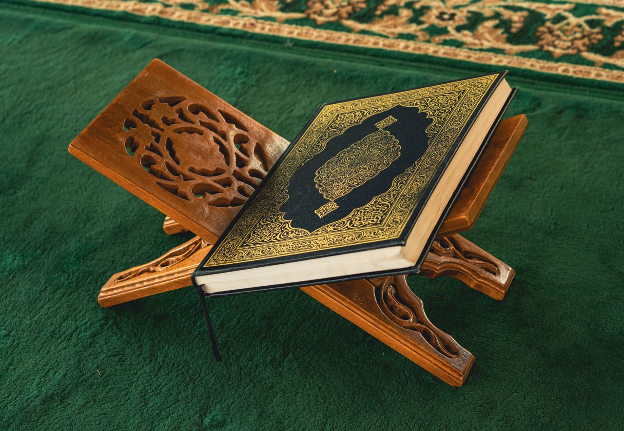 Close-up of the Quran resting on a carved wooden stand in a mosque setting.
